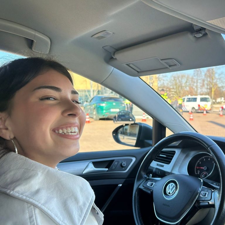 Jonge vrouw die vrolijk in een auto zit, met een stadsachtergrond.